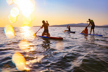 young people  riding  on sup surfing in the sea at sunset.