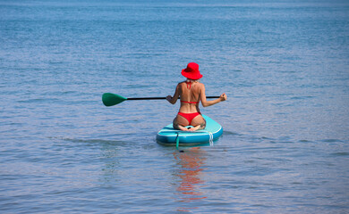 young women in red bikini  riding  on sup surfing in the sea at sumer time