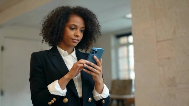 curly hair woman in blazer using blue smartphone indoors with natural lighting , curly hair woman using mobile phone hd video , 4k video , mp4 video , mov