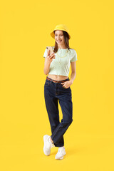 Smiling young woman in earphones using mobile phone on yellow background