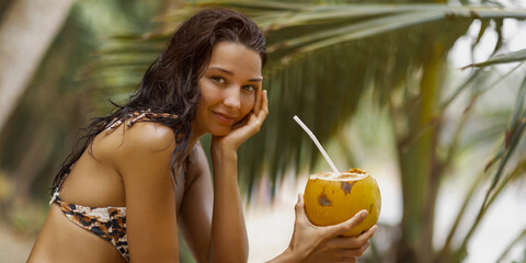 Beautiful Bikini Model Holding Coconut and Smiling in Tropical Setting © Buyanskyy Production