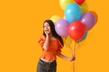 Surprised teenage girl with colorful air balloons on yellow background