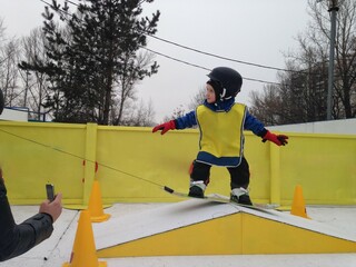 Young child learning snowboarding on a practice slope, wearing protective gear, helmet, and gloves,...