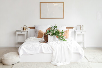 Comfortable bed, bedside tables and wicker basket with blooming jasmine flowers in interior of bedroom