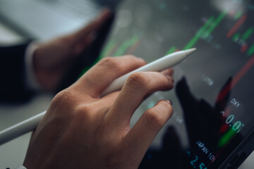 An investor monitors real-time stock market data on a smartphone and laptop, analyzing charts,...