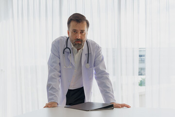 A serious and intense portrait of a male doctor standing in his office, representing authority and...