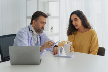 Orthopedist doctor explaining a knee joint condition to a female patient using an anatomical model....