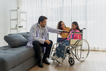 Caring doctor making a house call to encourage a young disabled girl in a wheelchair, with her...