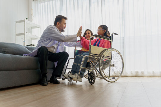 Caring doctor making a house call to encourage a young disabled girl in a wheelchair, with her mother's support. Home healthcare specialist showing test results on a tablet to a child