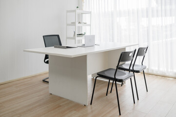 Modern and minimalist empty doctor's office or consultation room with a white desk and chairs....