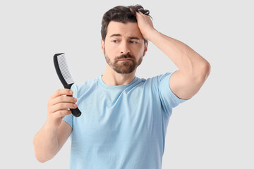 Man with comb on light background. Hair loss problem