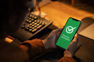 A person holding a smartphone that displays a Payment Successful confirmation screen after an...