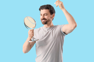 Happy man with mirror and serum for hair growth on blue background