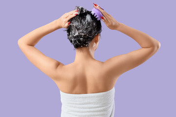 Pretty young Asian woman with scalp massage brush washing hair on lilac background, back view
