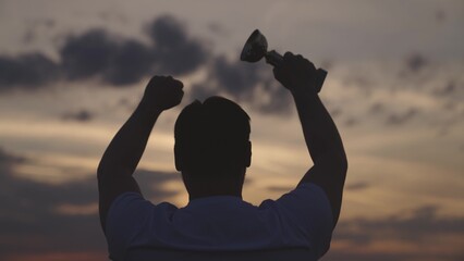 man with a cup rejoice at victory at sunset in the sky, silhouette of an athlete man, male...