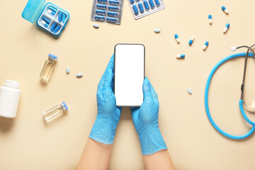 Doctor hands with mobile phone, medicines and stethoscope on beige background