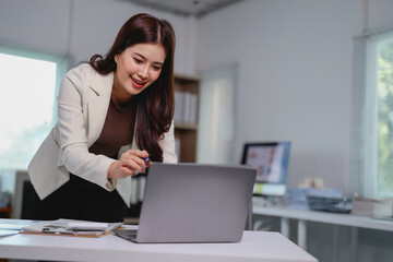 Young businesswoman pointing at her laptop screen while working at a bright, modern office desk,...