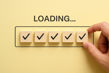 Wooden check mark block placed under the word LOADING on a minimalist background, symbolizing progress tracking, system update completion, or successful data transfer in digital workflow