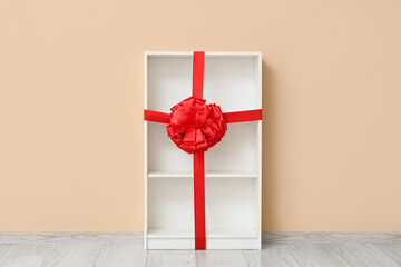 Empty bookshelf with gift bow near beige wall in room
