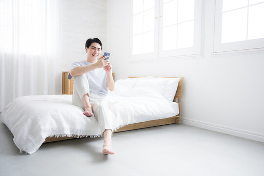 Whole body of thinking fresh man with smartphone relaxing on bed Copy space available