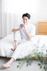 ベットでくつろぐスマホを持つ考える爽やかな男性の全身