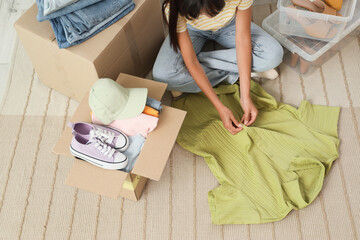 Young woman packing clothes for donation on carpet, top view