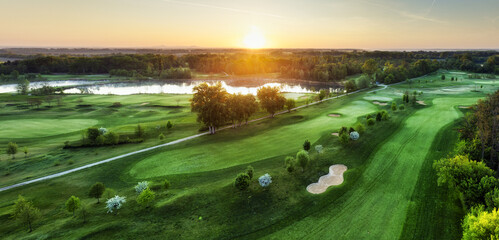 Obraz na płótnie Canvas Golf course at sunset with beautiful sky and sand trap. Scenic panoramic view of golf fairway with bunker from drone