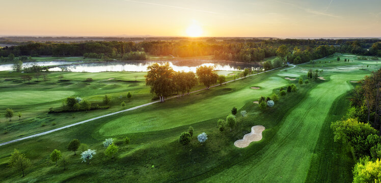 Fototapeta Golf course at sunset with beautiful sky and sand trap. Scenic panoramic view of golf fairway with bunker from drone