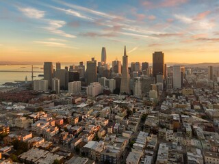 Aerial view of San Francisco, California, USA, at sunset. The photo shows the city skyline, including the Transamerica Pyramid and Salesforce Tower. The Bay Bridge is visible in the distance.