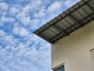 Corner of beige building with metal roof overhang against bright blue sky with scattered