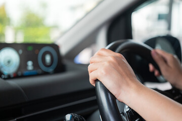 A car driver is holding and controlling on steering wheel of the modern car with digital display as background, close-up and selective focus a person hand. Transportation with people in action scene.