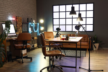 Interior of podcaster's studio with tables, sofa and glowing lamps at night