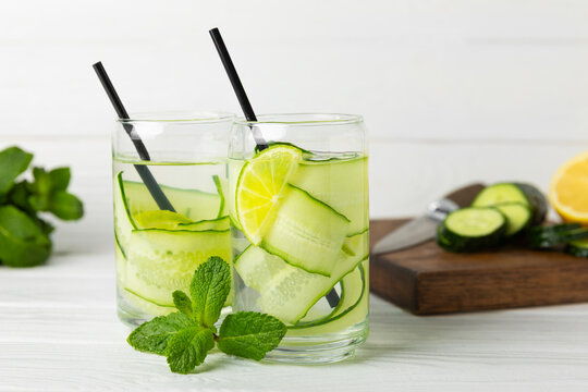 Cucumber water with lemon, lime and mint on a wooden table. Water infused with sliced ​​cucumber in a drinking glass. Tonic refreshing drink. Cucumber lemonade.Summer natural cooling drink.Copy space
