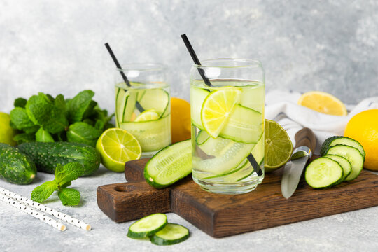 Cucumber water with lemon, lime and mint on a wooden table. Water infused with sliced ​​cucumber in a drinking glass. Tonic refreshing drink. Cucumber lemonade.Summer natural cooling drink.Copy space