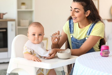 Young mother feeding her baby in high chair at home