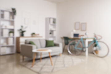 Blurred view of light home office with workplace, bicycle and sofa