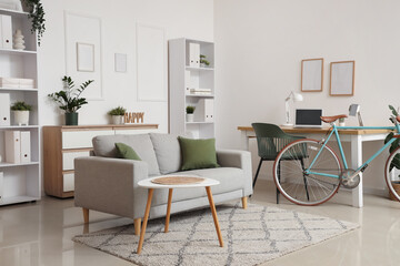 Interior of light home office with workplace, bicycle and sofa