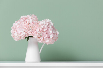 Vase with pink hydrangea flowers on shelf near green wall