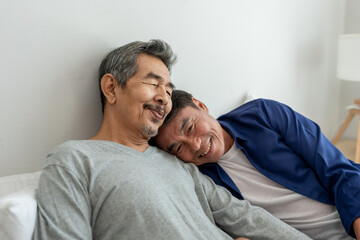 Asian elderly male gay couple lying down on bed and hugging each other.