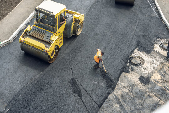 Workers lay a new asphalt coating using hot bitumen. Work of heavy machinery and paver. Top view