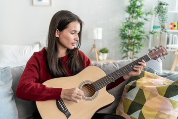 Fototapeta premium Mixed race beautiful young woman playing guitar in living room at home. 