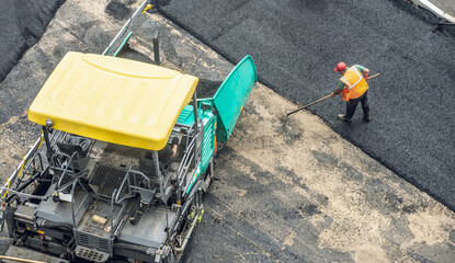 Workers lay a new asphalt coating using hot bitumen. Work of heavy machinery and paver. Top view