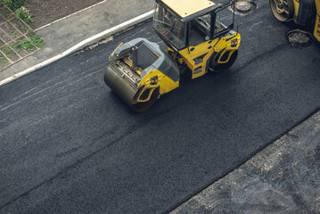 Workers lay a new asphalt coating using hot bitumen. Work of heavy machinery and paver. Top view