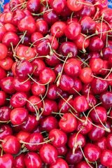 Close-up of a pile of fresh ripe red cherries with stems. Healthy organic fruit on sale at a local market. Bright and colorful food background.
