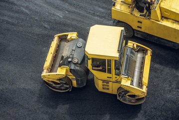 Workers lay a new asphalt coating using hot bitumen. Work of heavy machinery and paver. Top view