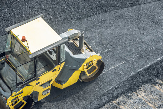 Workers lay a new asphalt coating using hot bitumen. Work of heavy machinery and paver. Top view