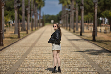 Young, beautiful, blonde woman, with leather jacket, snake miniskirt, boots and sunglasses, with...