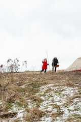 Exploring a snowy landscape, a child in a bright red coat walks alongside an adult while adventurous spirits embrace the chill of winter during their outdoor expedition