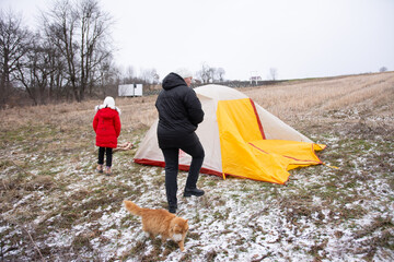 Family adventure unfolds as they set up a colorful tent on a chilly winter day in a serene field surrounded by bare trees