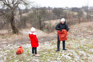 Bright winter adventure unfolds with a child and adult preparing gear in a snowy landscape surrounded by trees and distant hills
